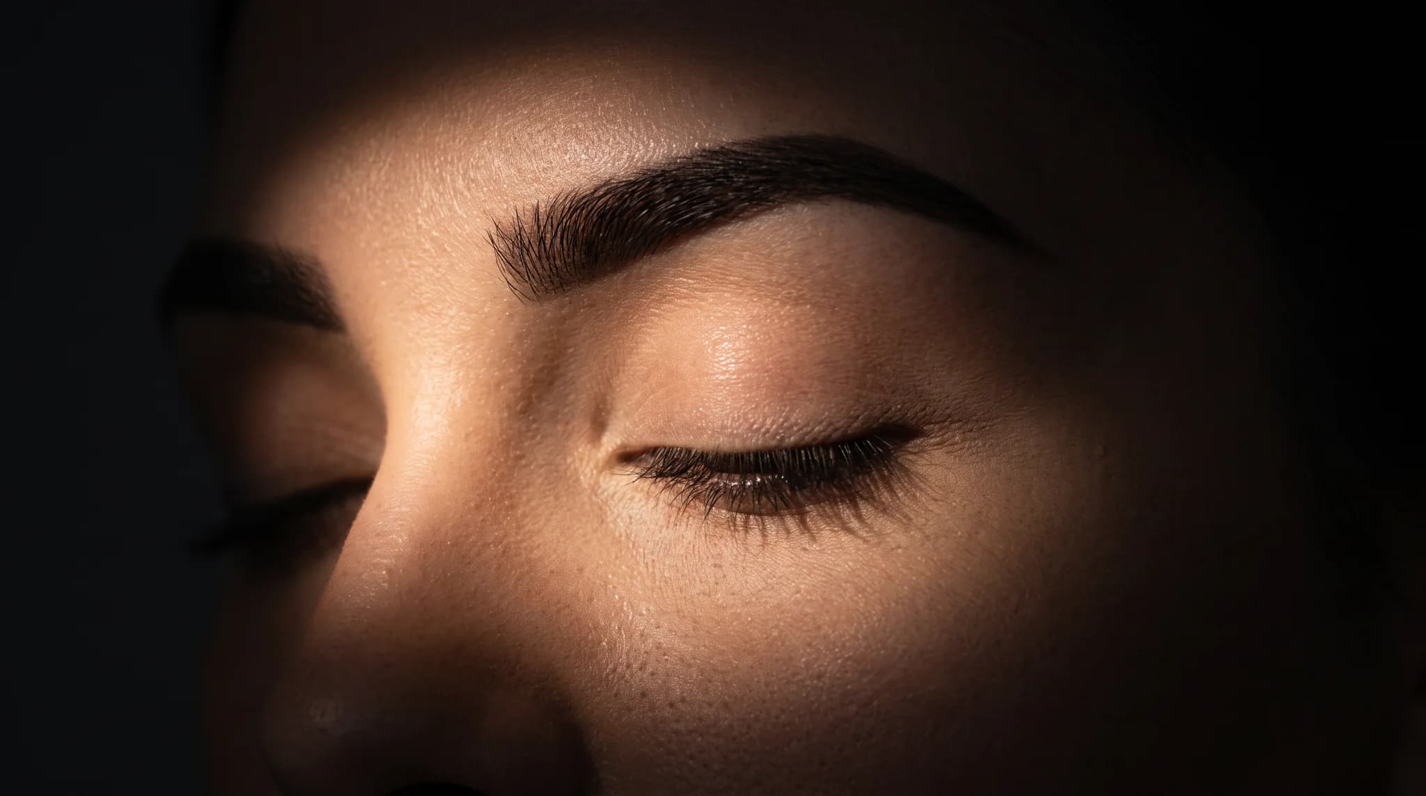 A perfect brow under a single beam of light, emerging from darkness