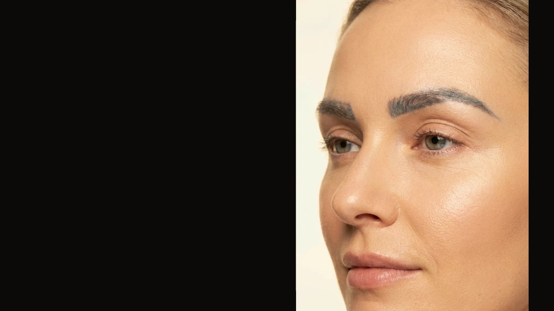 A woman with cool, blue-shifted brow pigment, photographed against warm ivory